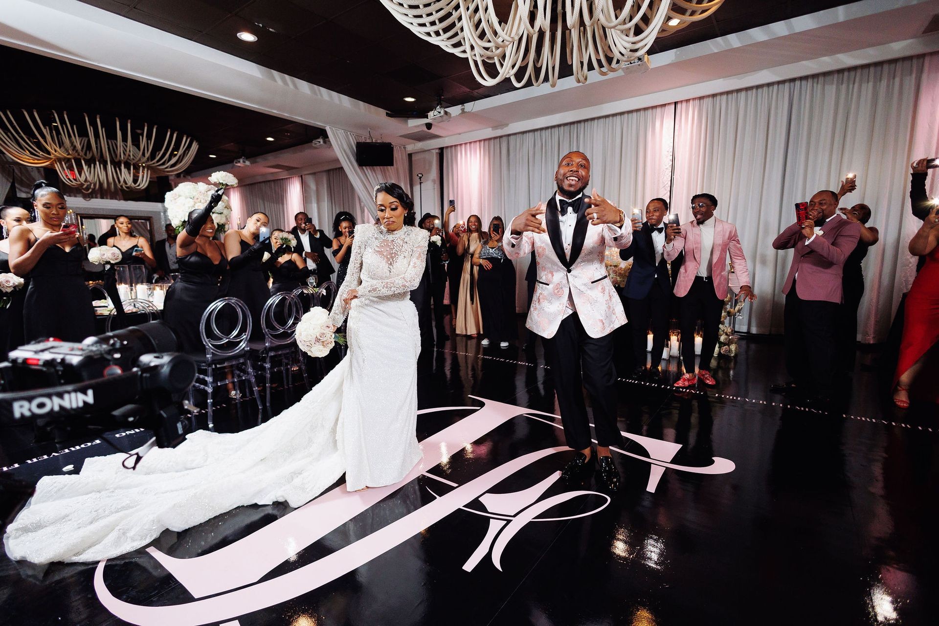 Bride and groom dancing at a wedding reception with guests taking photos and cheering them on.