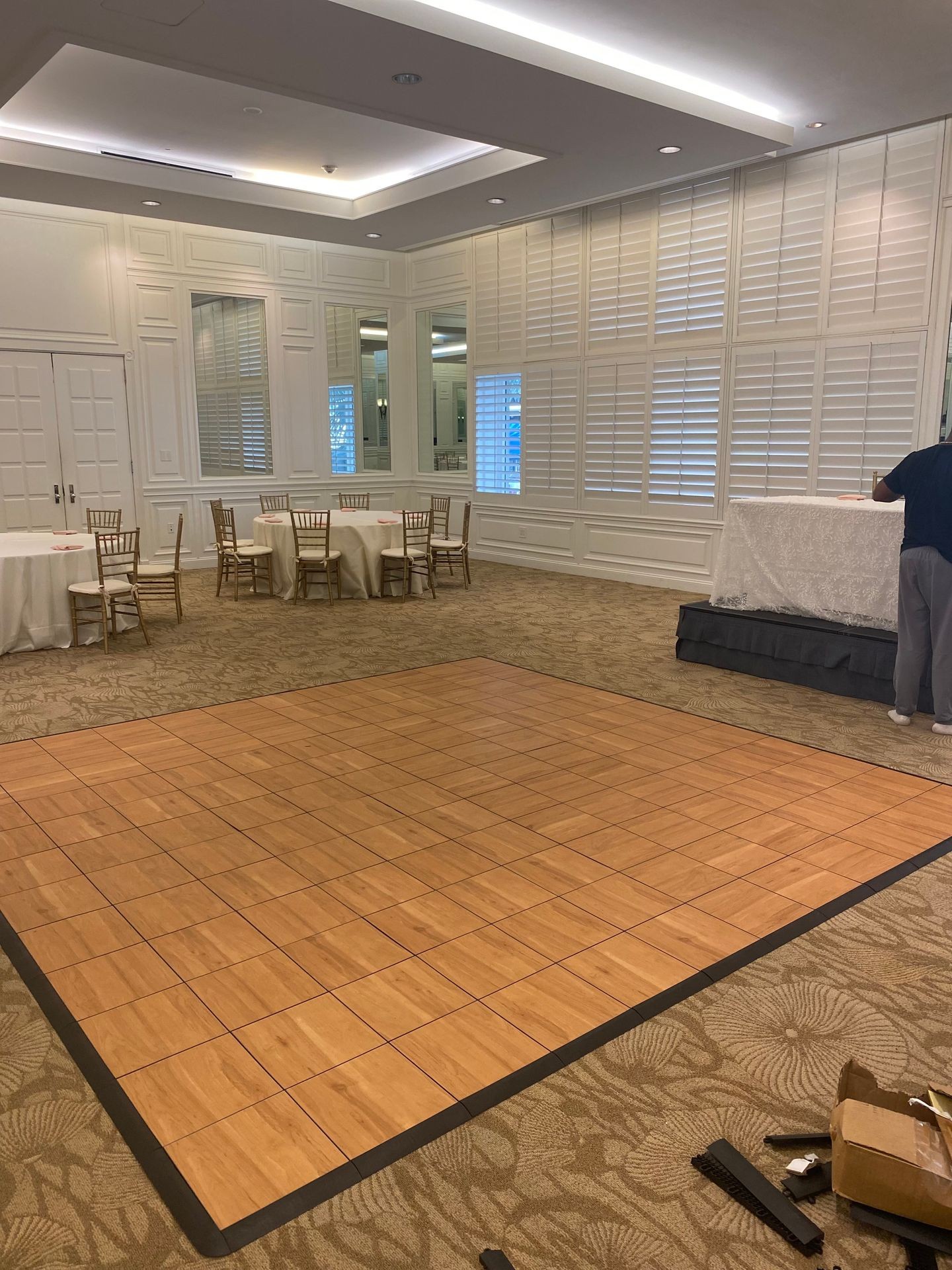 Empty event room with wooden dance floor, chairs, and tables set under bright ceiling lights.